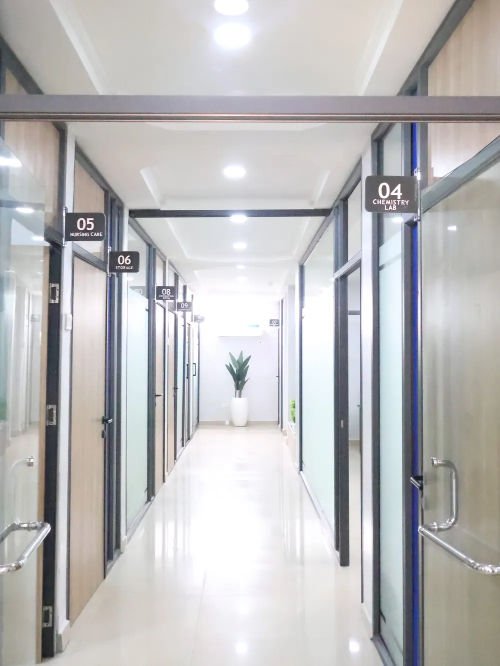 A clinic corridor lined with numbered department rooms: chemistry lab, nursing care, radiology, consulting room, and storage.